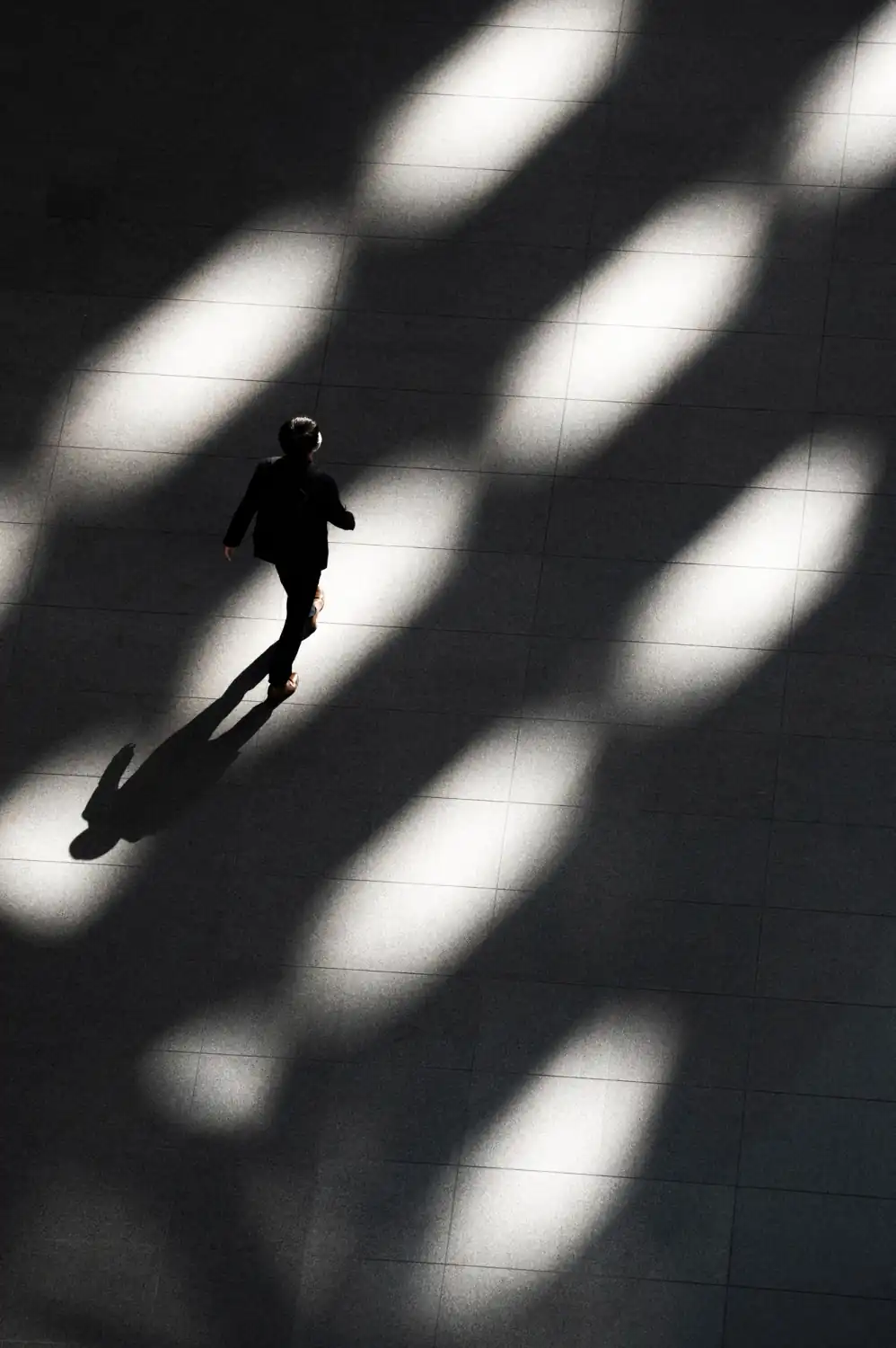 A person in a business suit walks across a floor with bright light and long shadows. The image reflects Dot&’s advisory, executive intelligence, and cybersecurity services.